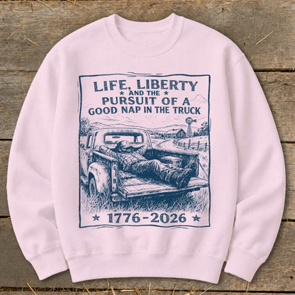Light pink sweatshirt with a graphic of a man napping in a truck, with text about life, liberty, and naps.