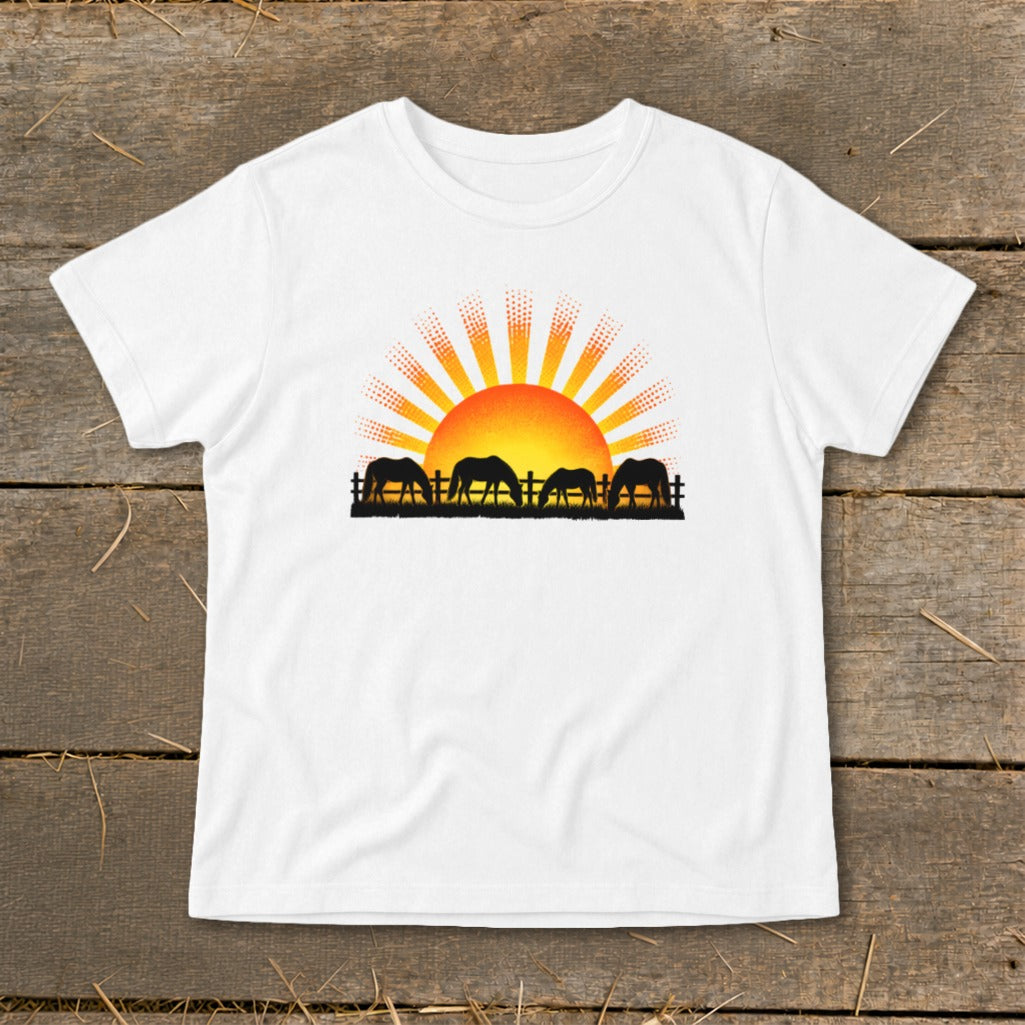Silhouette of horses grazing by a fence with a sunrise design on a white t-shirt.