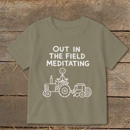 Green t-shirt with white text "OUT IN THE FIELD MEDITATING" and a stick figure on a tractor.