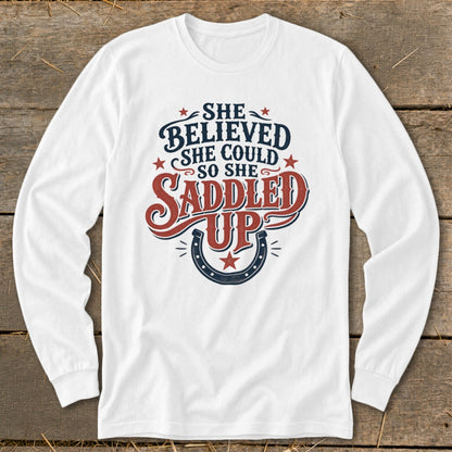 White long-sleeve shirt with "She believed she could so she saddled up" graphic.