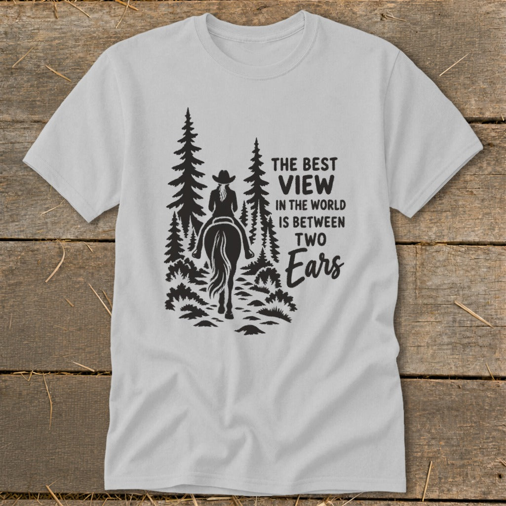 A light gray t-shirt with a black graphic of a horseback rider and pine trees alongside text reading, The best view in the world is between two ears.
