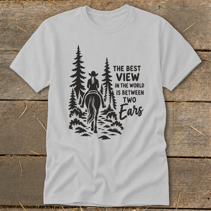 A light gray t-shirt with a black graphic of a horseback rider and pine trees alongside text reading, The best view in the world is between two ears.