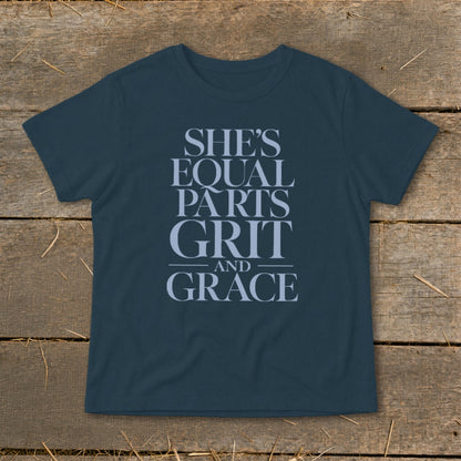 Dark blue t-shirt with light blue text reading "SHE'S EQUAL PARTS GRIT AND GRACE".