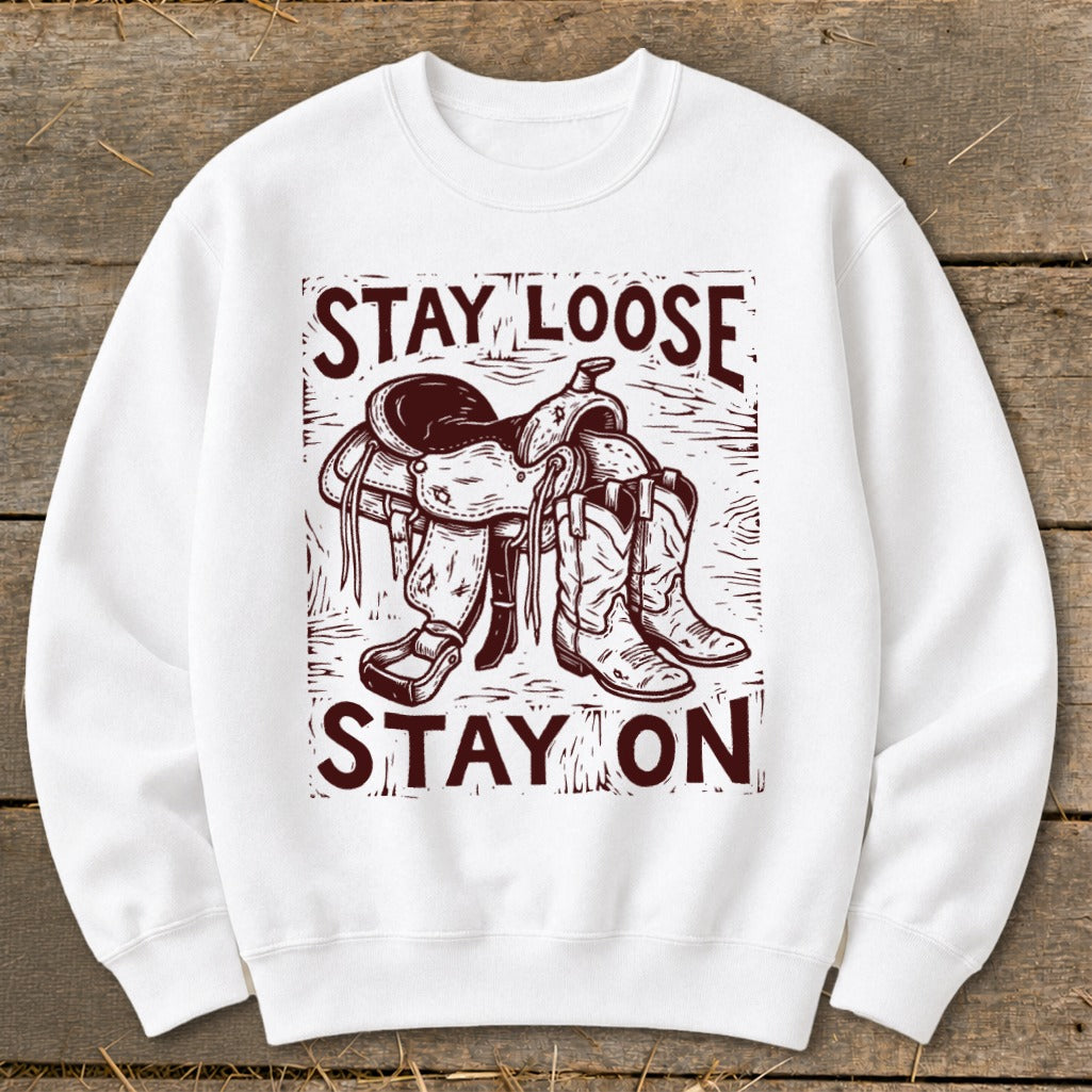 White sweatshirt with maroon graphic of saddle and cowboy boots, text "STAY LOOSE STAY ON".