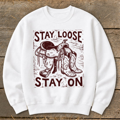 White sweatshirt with maroon graphic of saddle and cowboy boots, text "STAY LOOSE STAY ON".