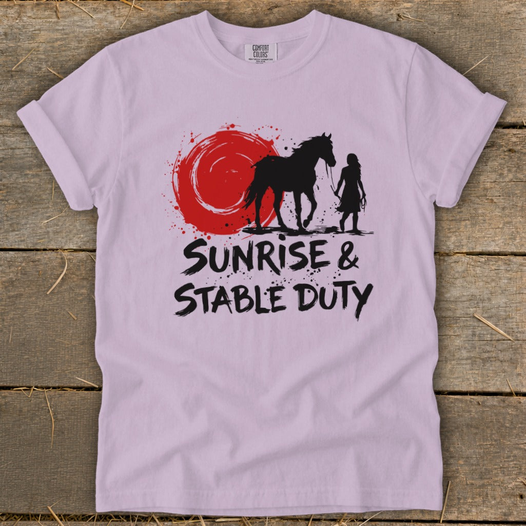 Light purple t-shirt with black silhouette of horse and person, red sunburst, and text "SUNRISE & STABLE DUTY".