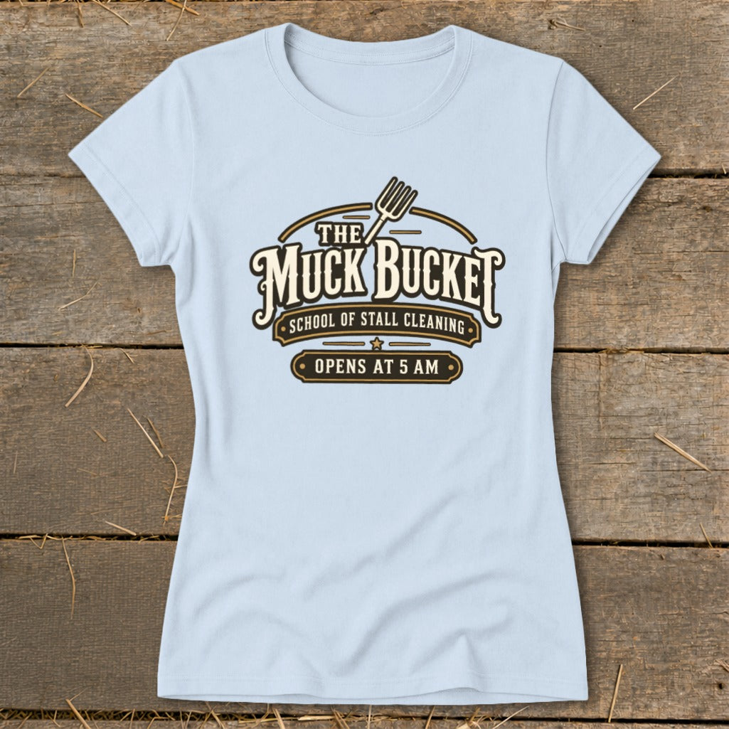 Light blue t-shirt with "The Muck Bucket School of Stall Cleaning Opens at 5 AM" logo.