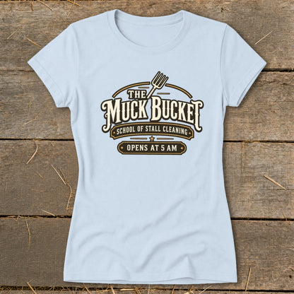 Light blue t-shirt with "The Muck Bucket School of Stall Cleaning Opens at 5 AM" logo.