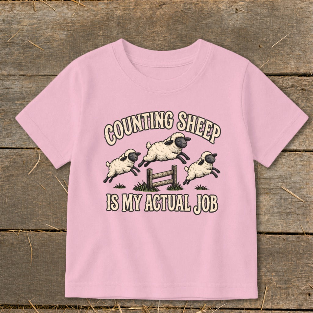Pink t-shirt with "Counting Sheep Is My Actual Job" and three jumping sheep illustration.