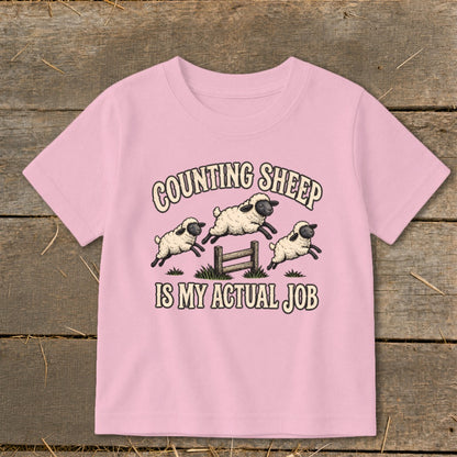 Pink t-shirt with "Counting Sheep Is My Actual Job" and three jumping sheep illustration.