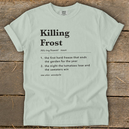 A light green t-shirt with black dictionary-style text defining the phrase Killing Frost laid flat on wooden planks.