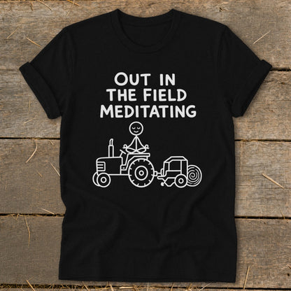 Black t-shirt with white text "Out in the field meditating" and stick figure on a tractor.