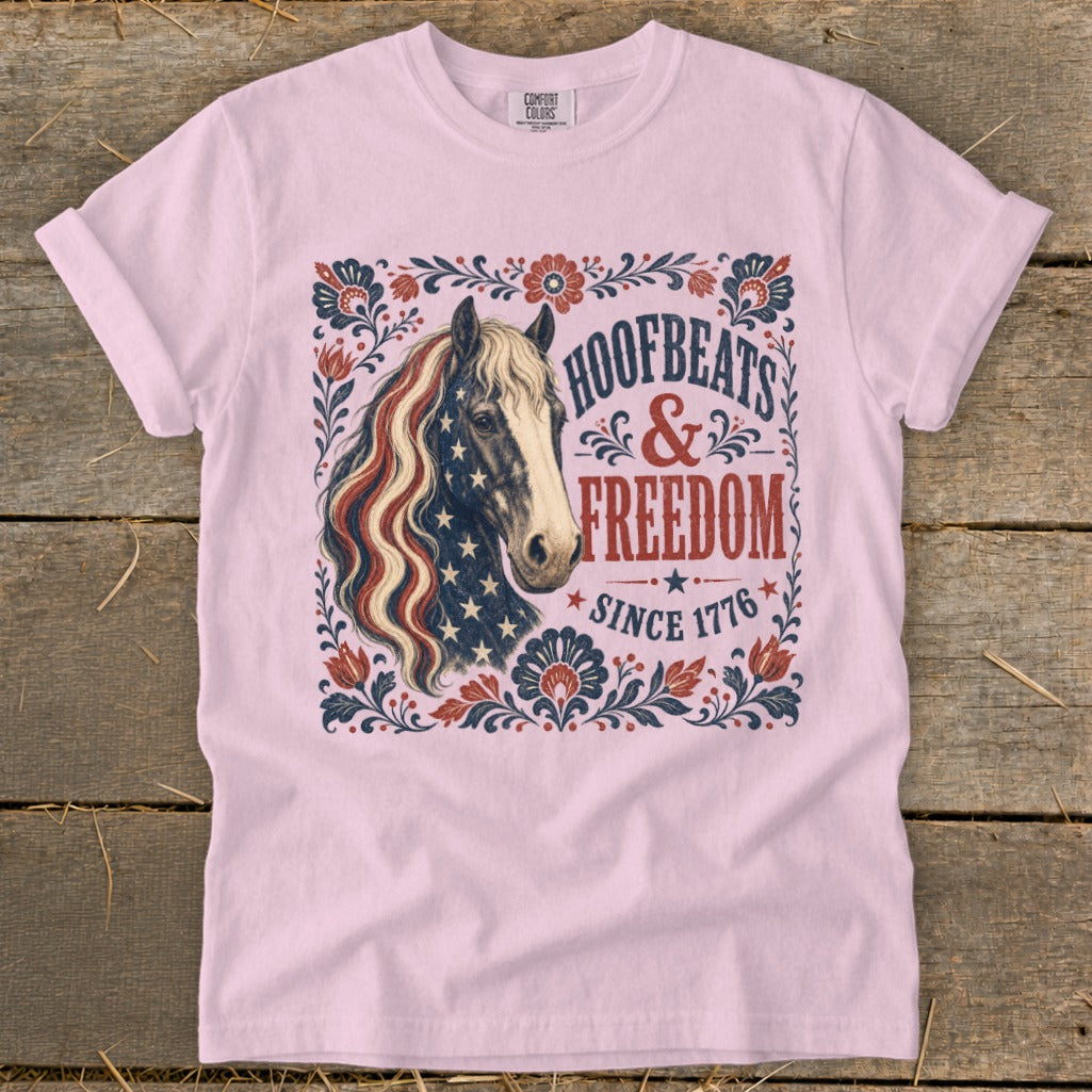 Pink t-shirt with a horse featuring an American flag mane, "Hoofbeats & Freedom Since 1776" text.