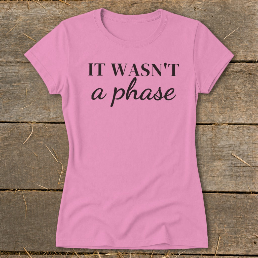 Pink t-shirt with black text "IT WASN'T a phase" on a wooden background.