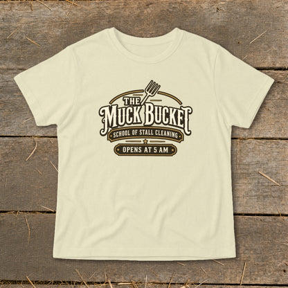 Cream t-shirt with "The Muck Bucket School of Stall Cleaning Opens at 5 AM" logo.