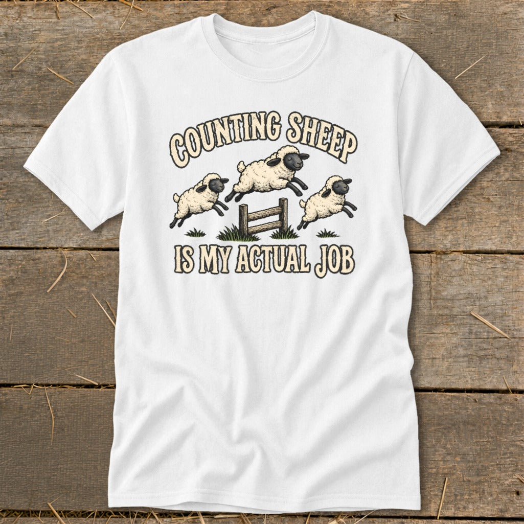 White t-shirt with cartoon sheep jumping over a fence and text "Counting Sheep is my actual job".