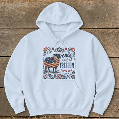 White hoodie with a graphic of a sheep with an American flag pattern, text "FLOCKS & FREEDOM SINCE 1776".