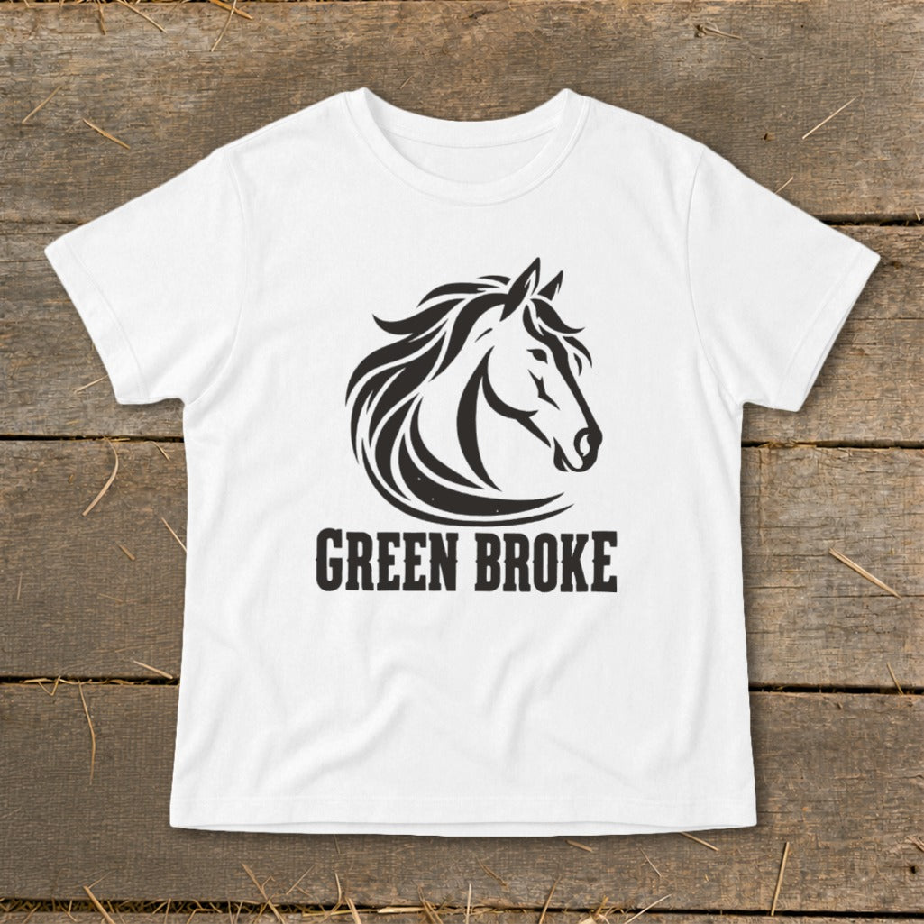 A white t-shirt featuring a black graphic of a horse head and the text GREEN BROKE, laid flat on a wooden surface.
