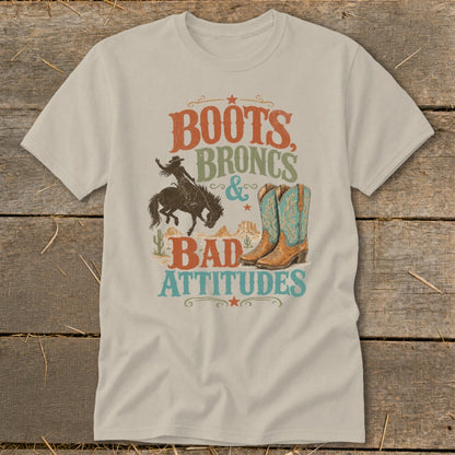 T-shirt graphic with text "Boots, Broncs & Bad Attitudes," cowboy, boots, and desert landscape.