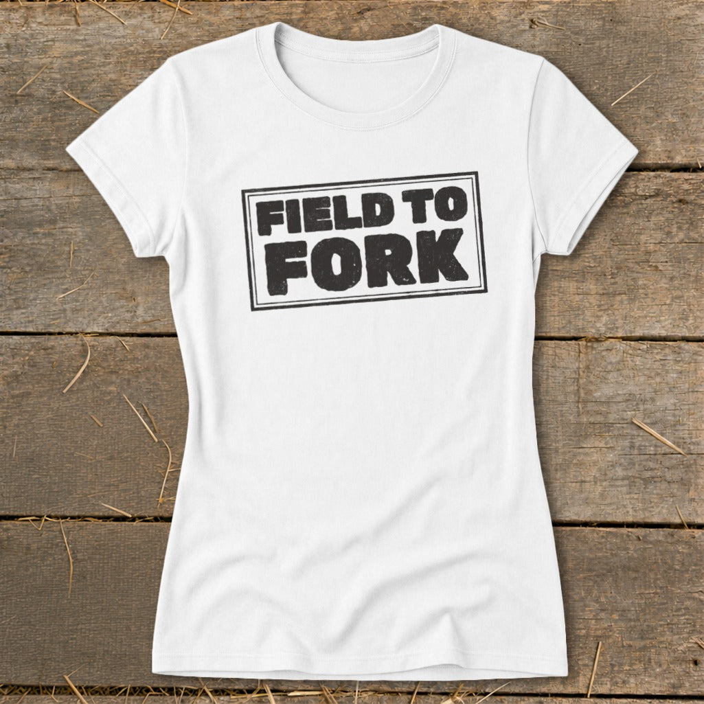 A white women's crew neck t-shirt featuring the black text "FIELD TO FORK" inside a rectangle.