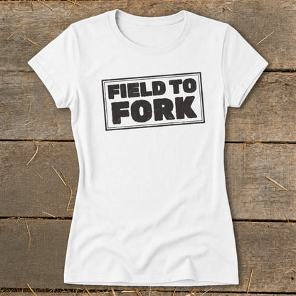 A white women's crew neck t-shirt featuring the black text "FIELD TO FORK" inside a rectangle.
