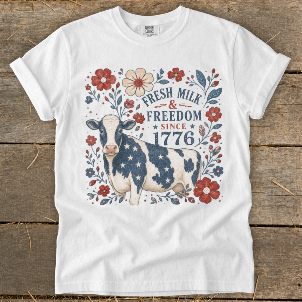 White t-shirt with a cow wearing a star-spangled pattern and text "Fresh Milk & Freedom Since 1776".