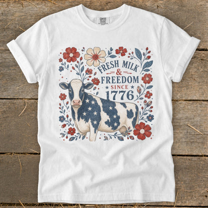White t-shirt with a cow wearing a star-spangled pattern and text "Fresh Milk & Freedom Since 1776".