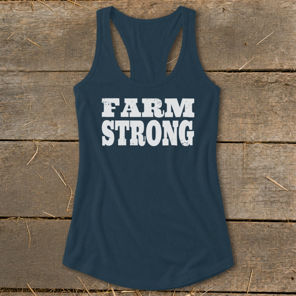 Dark blue racerback tank top with the distressed white text "FARM STRONG" on a wooden background.
