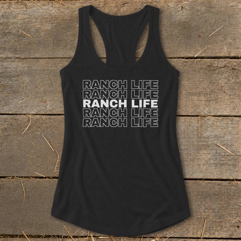 A black racerback tank top with repeated white text reading Ranch Life laid flat on wooden boards.
