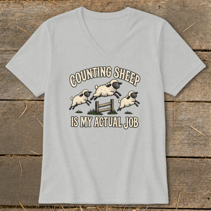 Grey v-neck t-shirt with cartoon sheep jumping over a fence with "Counting Sheep Is My Actual Job" text.
