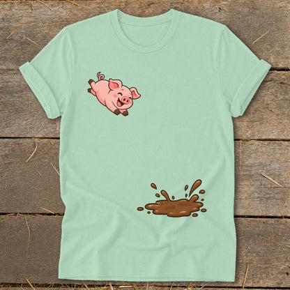Light green t-shirt with a cartoon pig jumping over a splatter of mud.