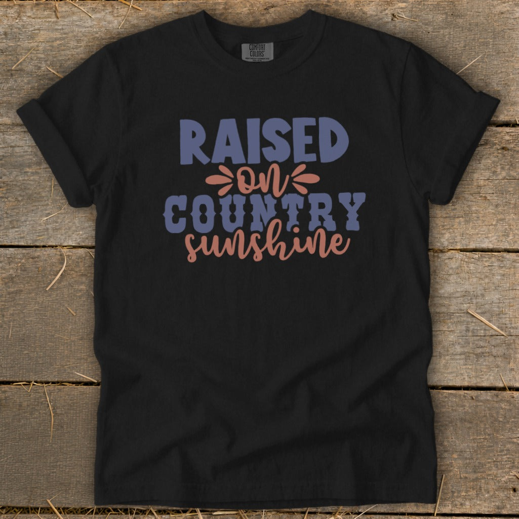 Black t-shirt with "Raised on Country Sunshine" text in blue, pink, and purple.