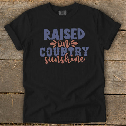 Black t-shirt with "Raised on Country Sunshine" text in blue, pink, and purple.