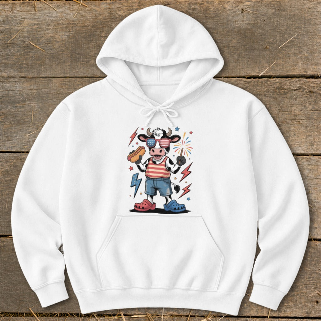 Cartoon cow wearing American flag shirt, sunglasses, and holding hot dog and firework.