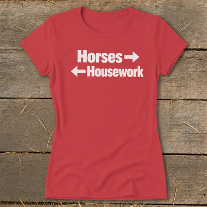 A red women's t-shirt with white text reading Horses and Housework laid flat on wood.