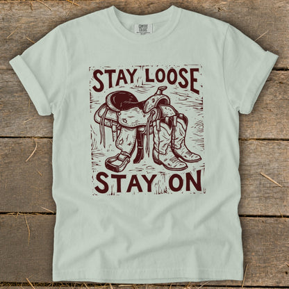 Light green t-shirt with "STAY LOOSE STAY ON" text and cowboy saddle and boots graphic.