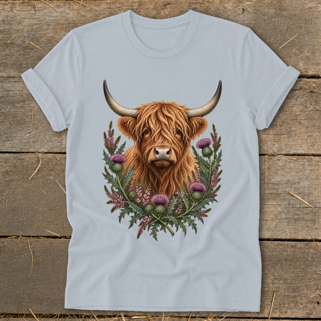Highland cow portrait surrounded by thistles and heather on a light blue t-shirt.