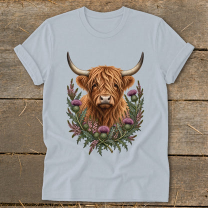 Highland cow portrait surrounded by thistles and heather on a light blue t-shirt.