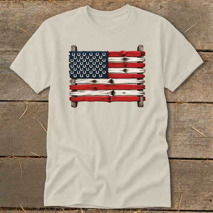 A cream-colored short-sleeved t-shirt features a graphic of the American flag made of weathered wood and horseshoes.