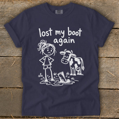 A dark blue t-shirt with a white graphic of a stick-figure girl and a cow standing by a boot in mud, with the text "lost my boot again".