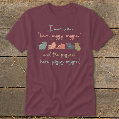 Maroon t-shirt with text "I was like "here piggy piggies" and the piggies here piggy piggied" and row of cartoon pigs.