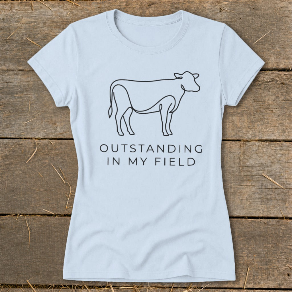 Light blue t-shirt with black line drawing of a cow and text "OUTSTANDING IN MY FIELD".