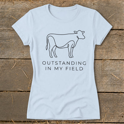 Light blue t-shirt with black line drawing of a cow and text "OUTSTANDING IN MY FIELD".