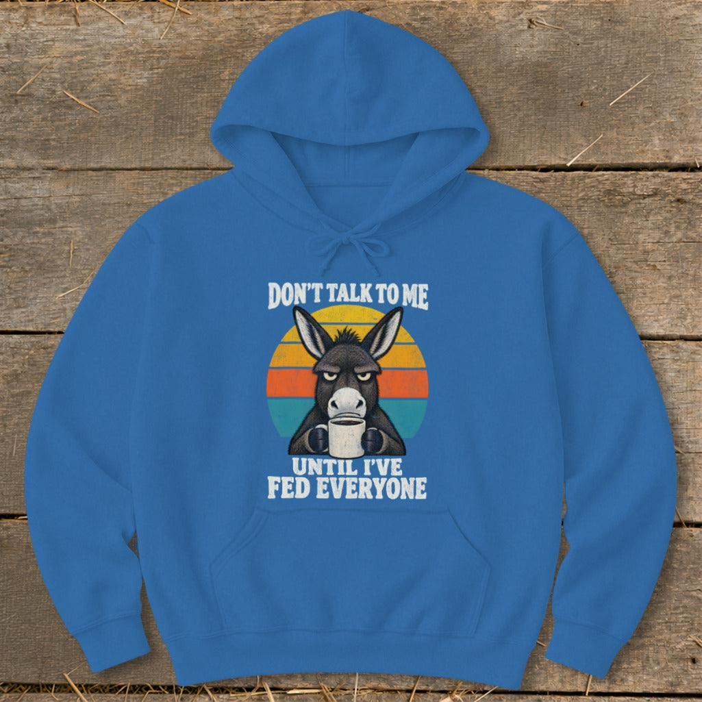 Blue pullover hoodie featuring a grumpy donkey drinking coffee graphic and the text Don't Talk To Me Until I've Fed Everyone.