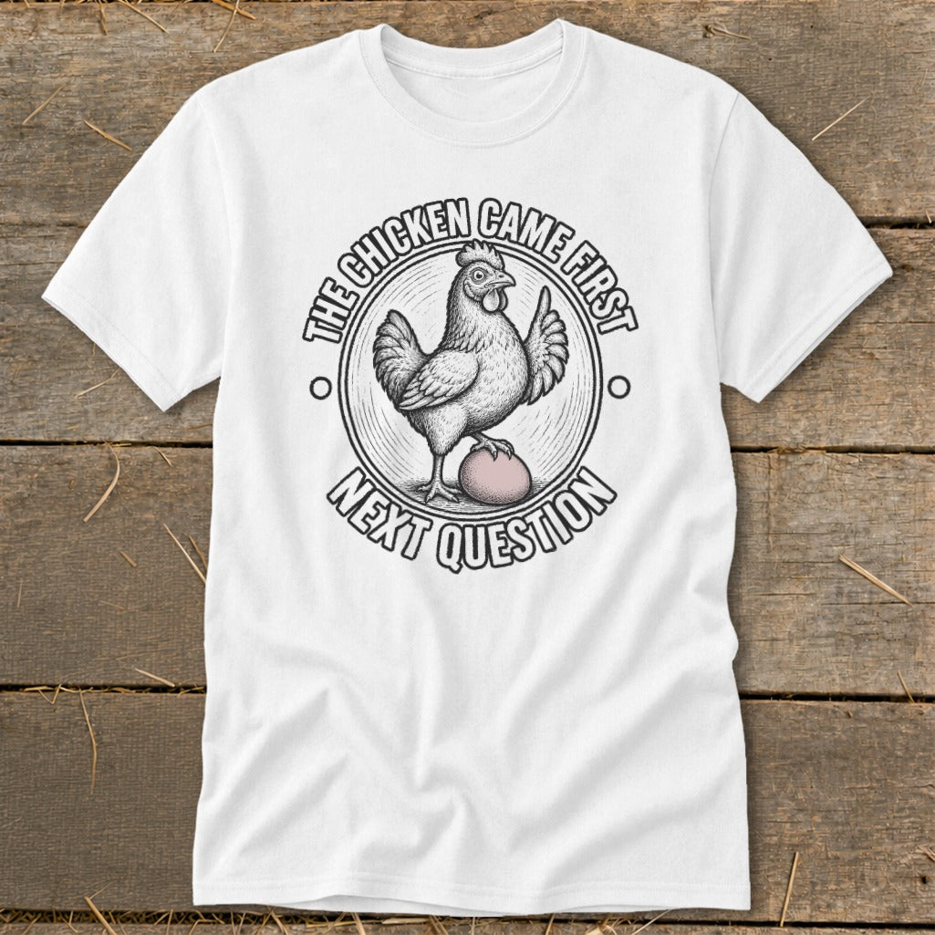 White t-shirt graphic with a chicken on an egg and text reading "The Chicken Came First Next Question."