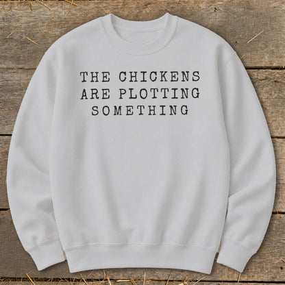 White sweatshirt with black text "The chickens are plotting something".