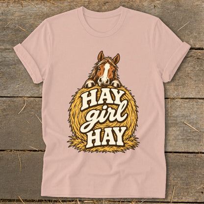 Pink t-shirt with a horse peeking over a hay bale, text "HAY girl HAY".