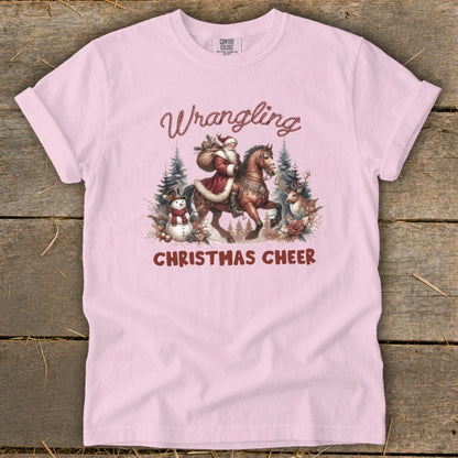Pink t-shirt with "Wrangling Christmas Cheer" and Santa riding a horse with a snowman and deer.