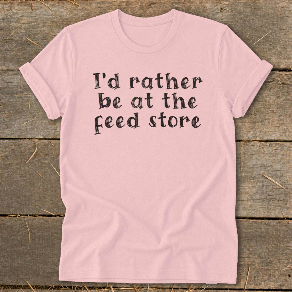 Pink t-shirt with black text reading "I'd rather be at the feed store".