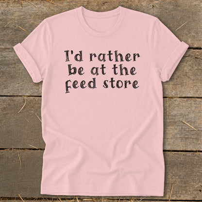 Pink t-shirt with black text reading "I'd rather be at the feed store".